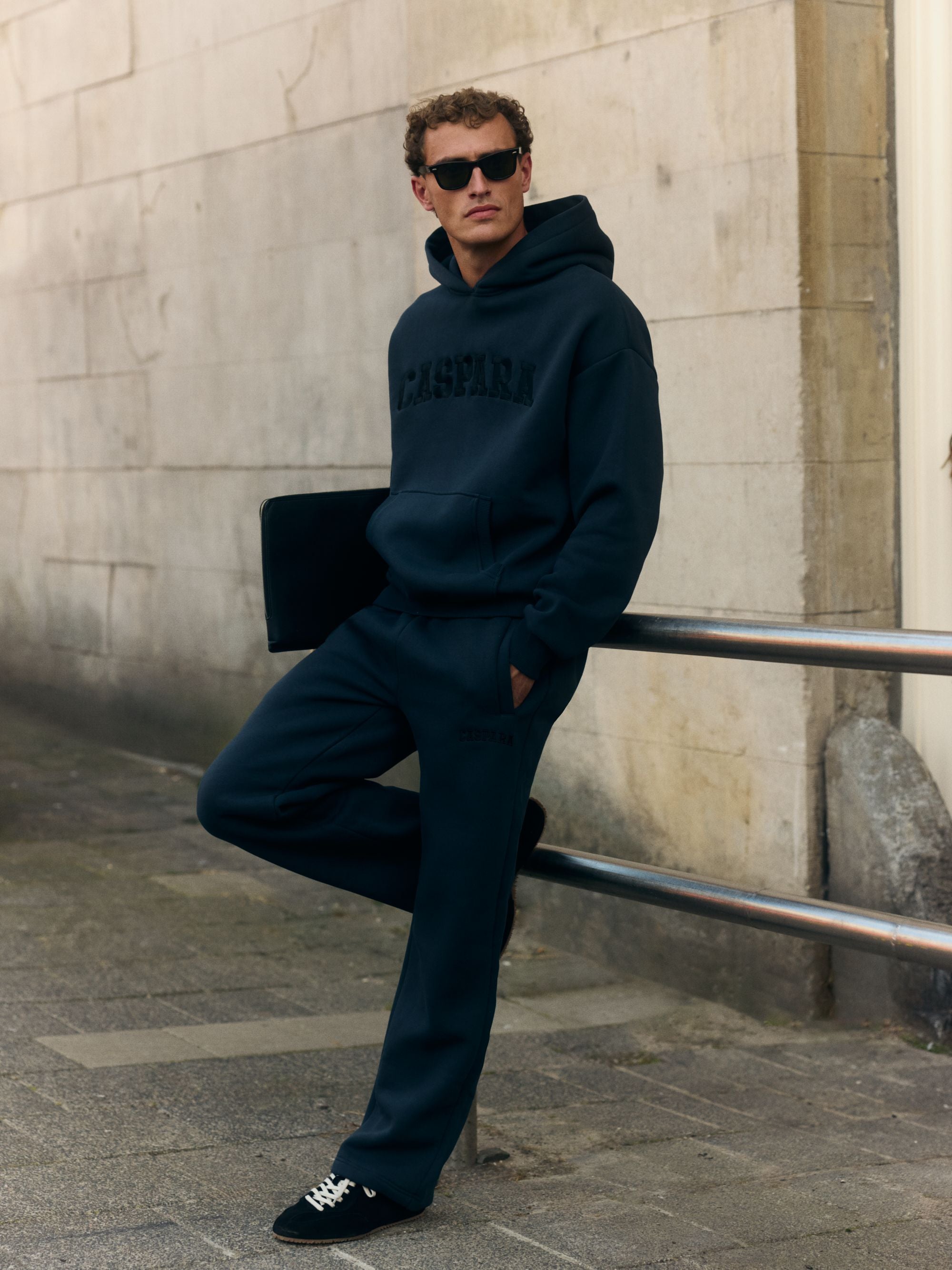 Man wearing a navy CASPARA logo hoodie and matching sweatpants with sunglasses outdoors.